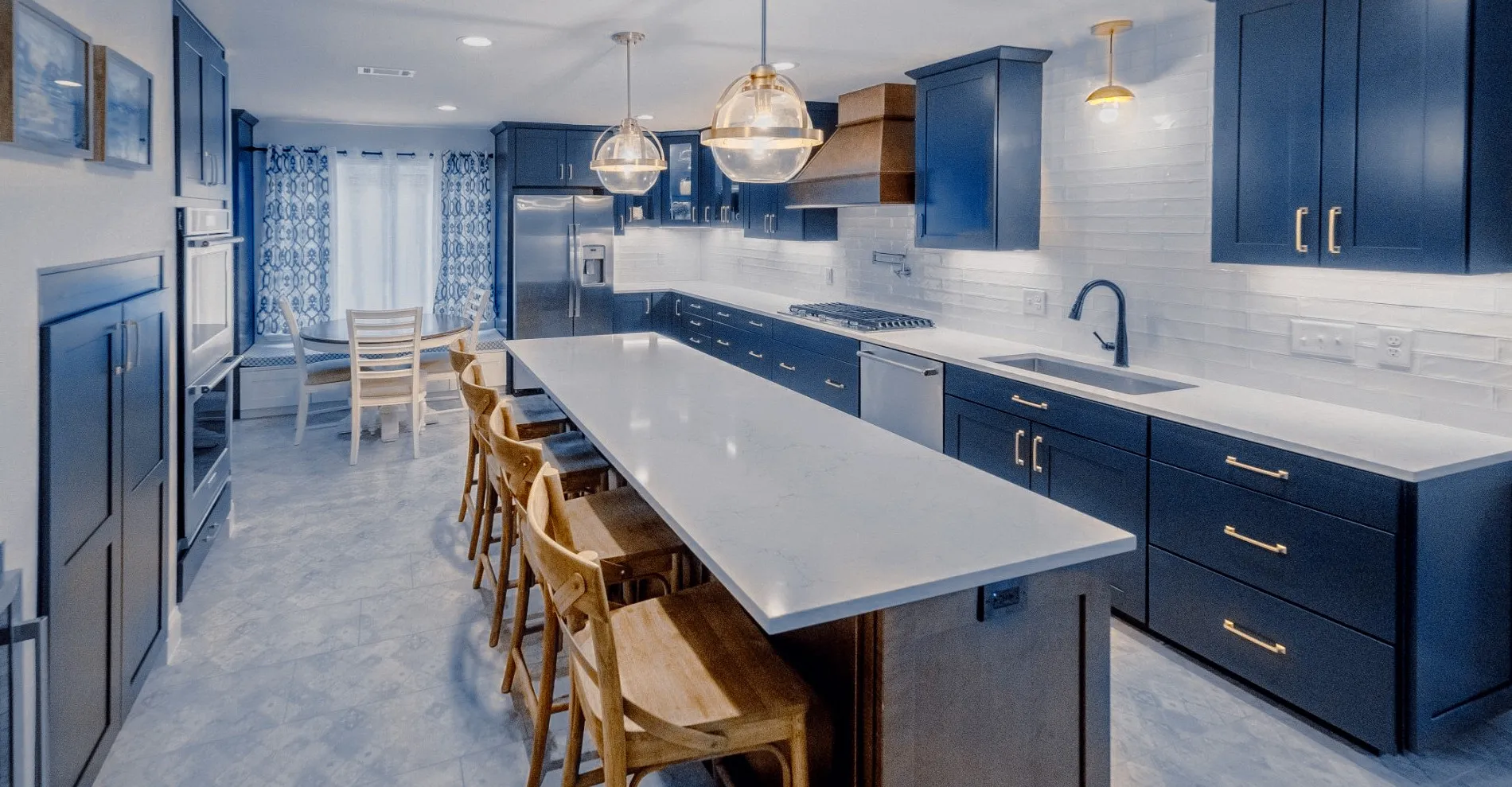 Remodeled Fort Worth kitchen by The Rockaway Company with navy shaker cabinetry, brass hardware, a long quartz island and pendant lighting